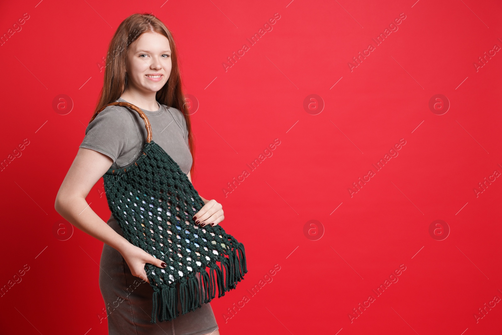 Photo of Teenage girl with handmade macrame bag on red background. Space for text