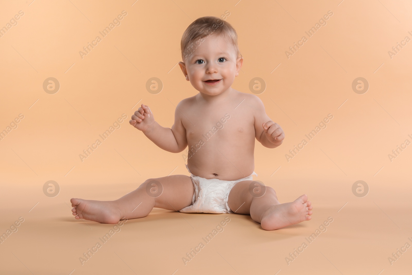 Photo of Cute little baby in diaper sitting on beige background