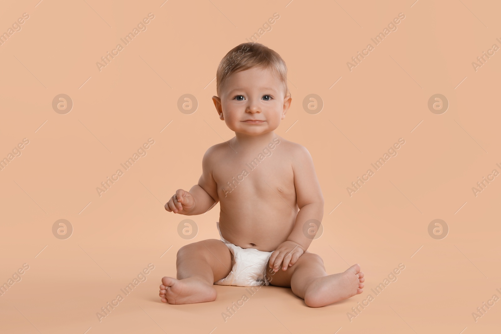 Photo of Cute little baby in diaper sitting on beige background