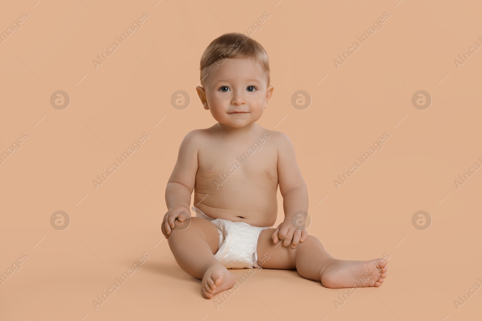 Photo of Cute little baby in diaper sitting on beige background