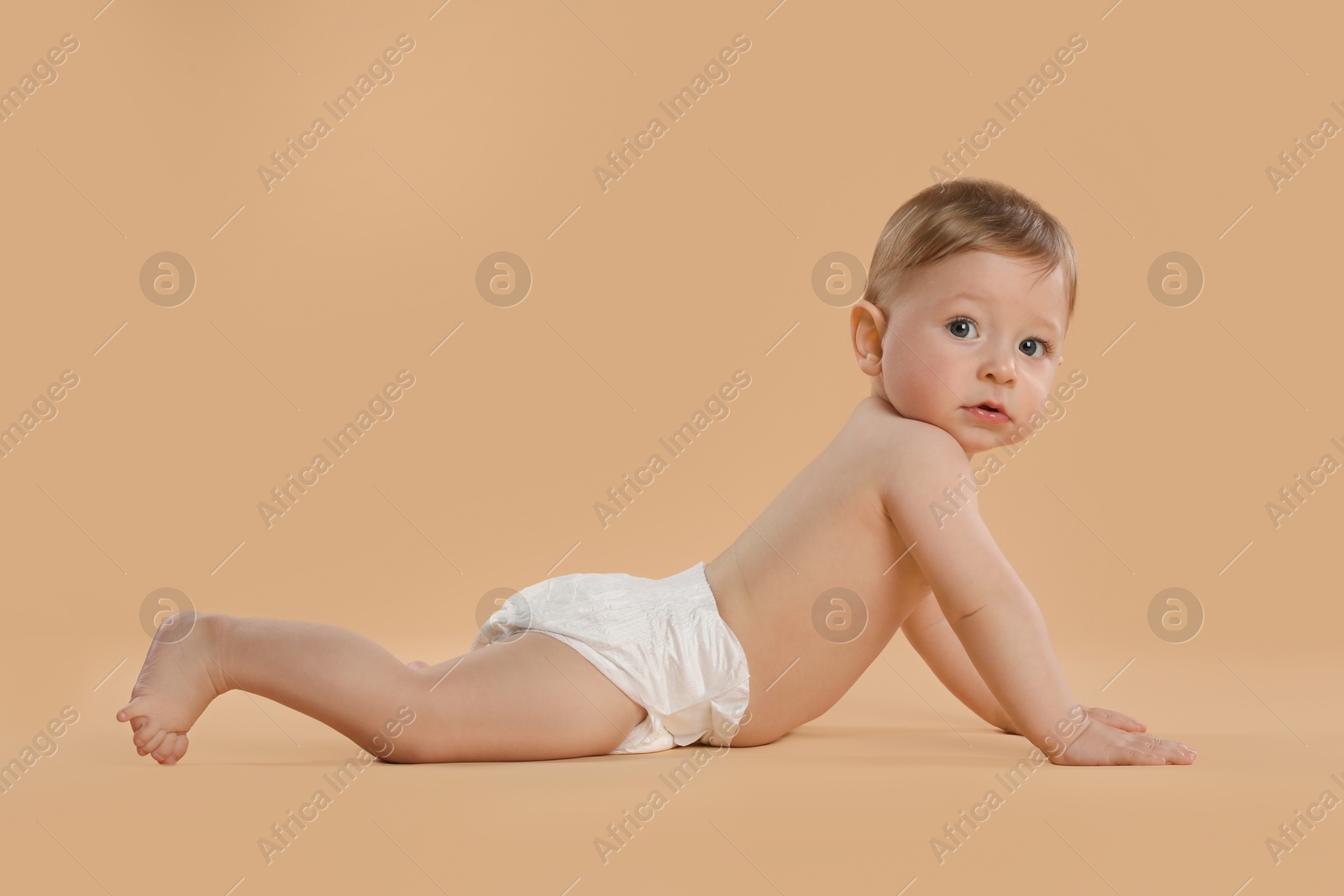 Photo of Cute little baby in diaper crawling on beige background