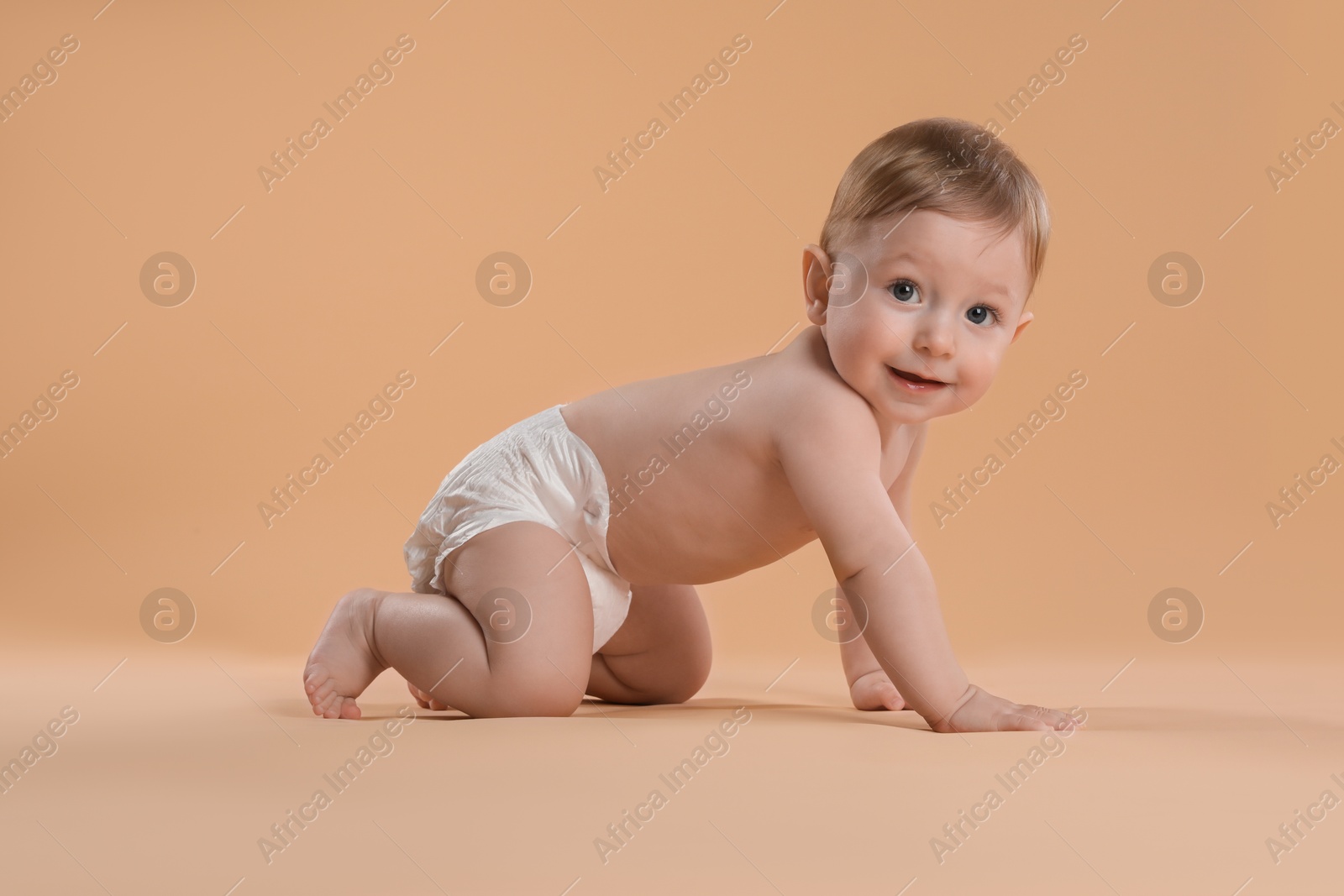 Photo of Cute little baby in diaper crawling on beige background