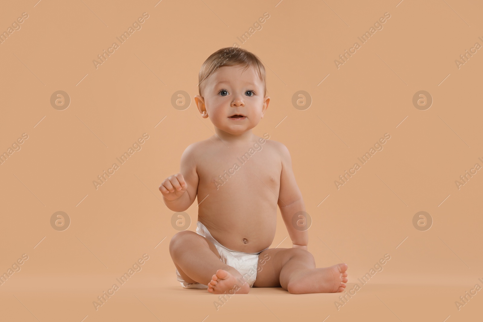 Photo of Cute little baby in diaper sitting on beige background