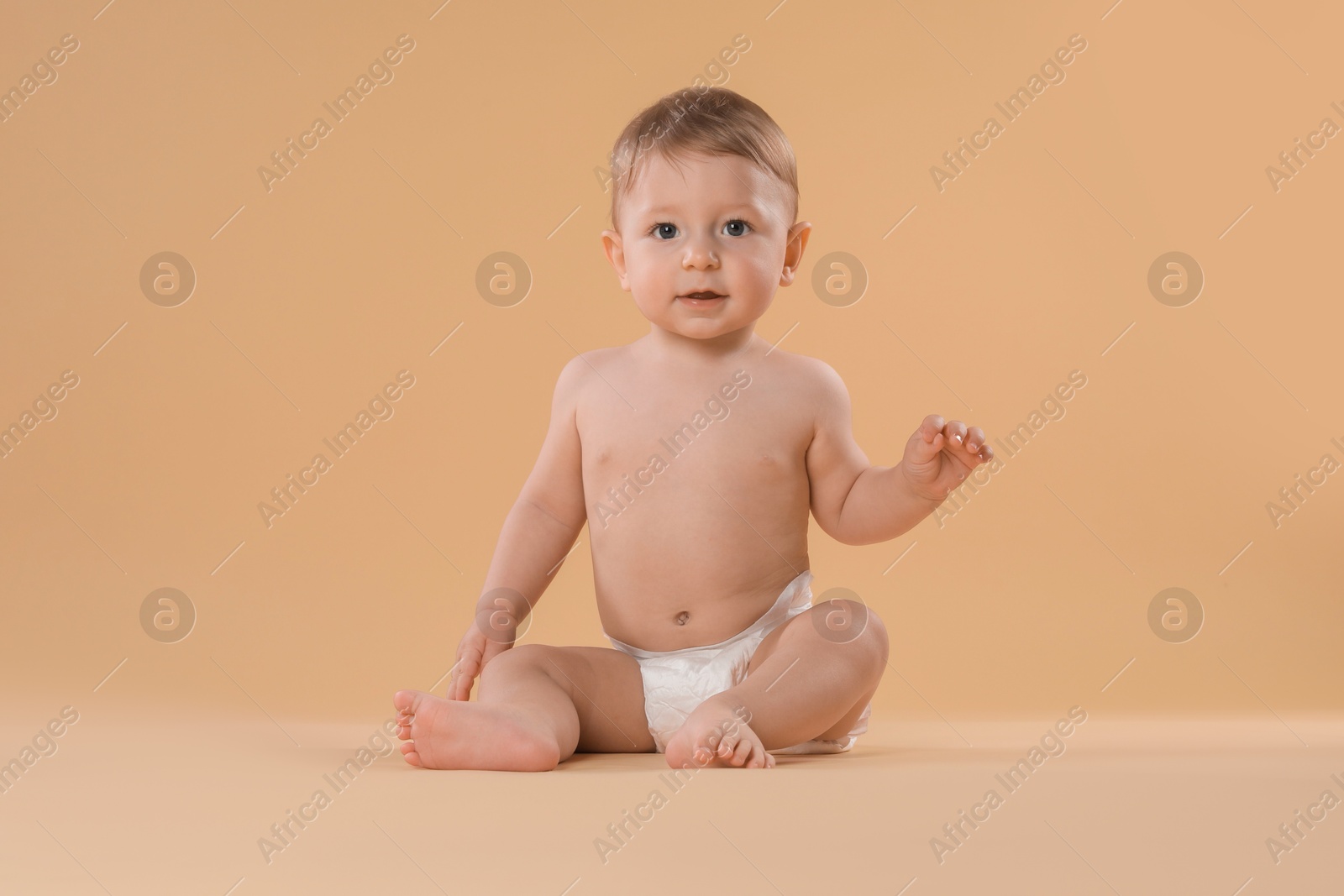 Photo of Cute little baby in diaper sitting on beige background