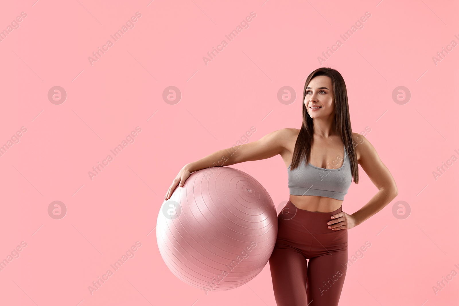 Photo of Woman in gym clothes with fitness ball on pink background