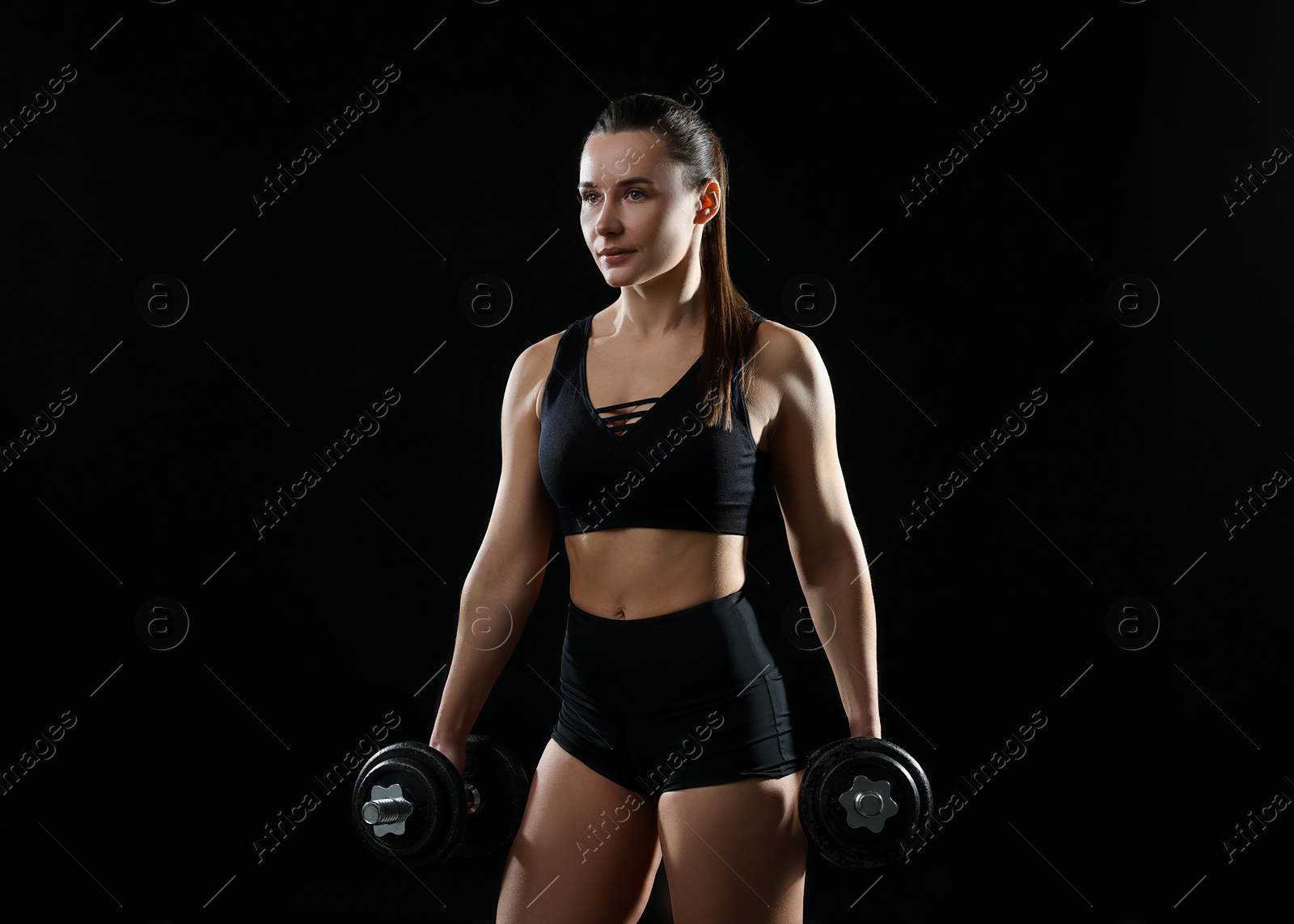 Photo of Beautiful woman in sportswear training with barbells on black background. Space for text