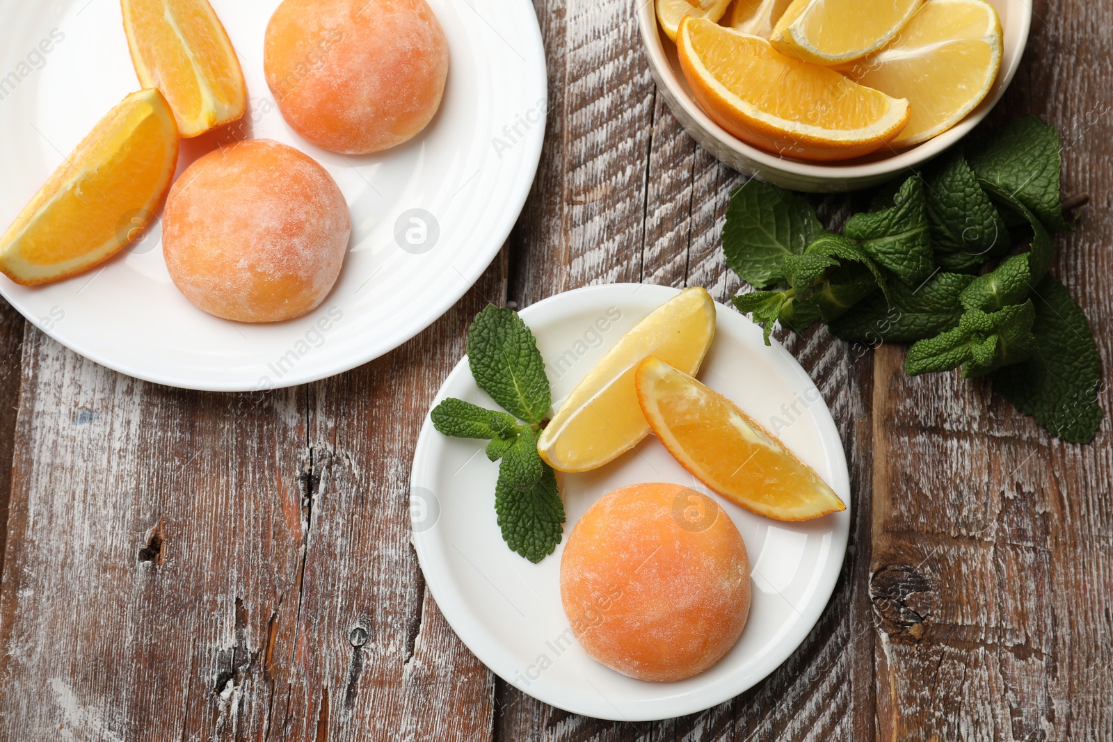 Photo of Tasty mochi, cut orange and mint on wooden table, flat lay