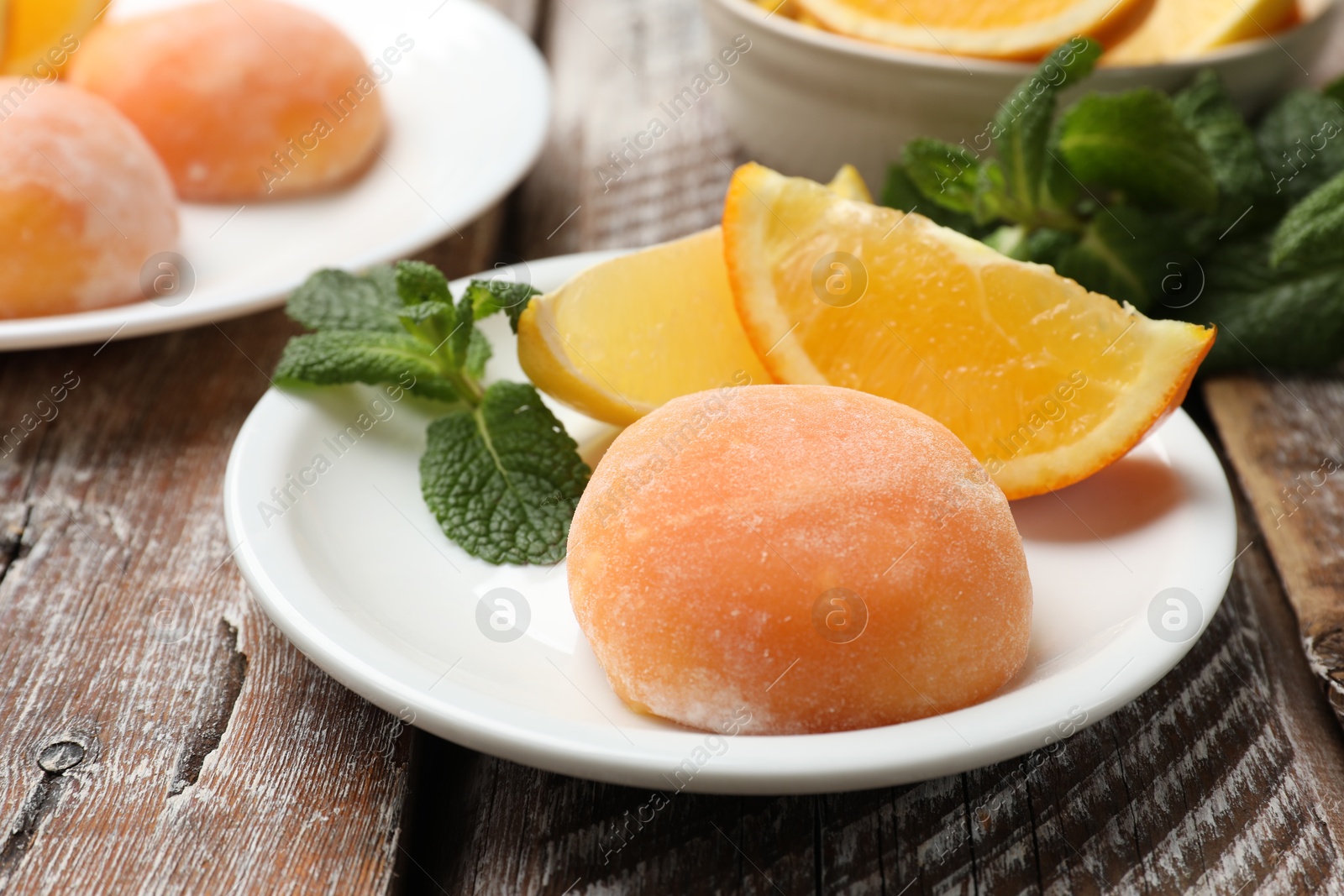 Photo of Plate with tasty mochi, cut orange and mint on wooden table, closeup