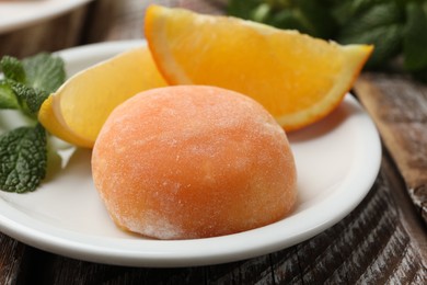 Photo of Plate with tasty mochi, cut orange and mint on wooden table, closeup