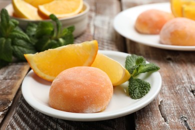 Photo of Plate with tasty mochi, cut orange and mint on wooden table, closeup