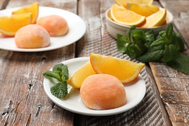 Photo of Plate with tasty mochi, cut orange and mint on wooden table, closeup