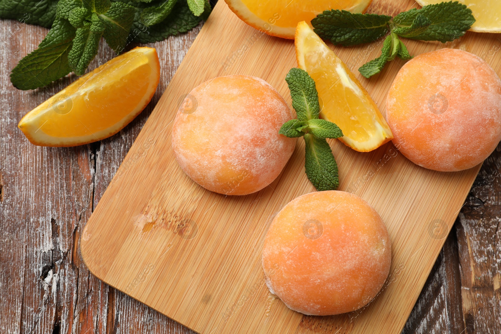 Photo of Board with tasty mochi, cut orange and mint on wooden table, flat lay