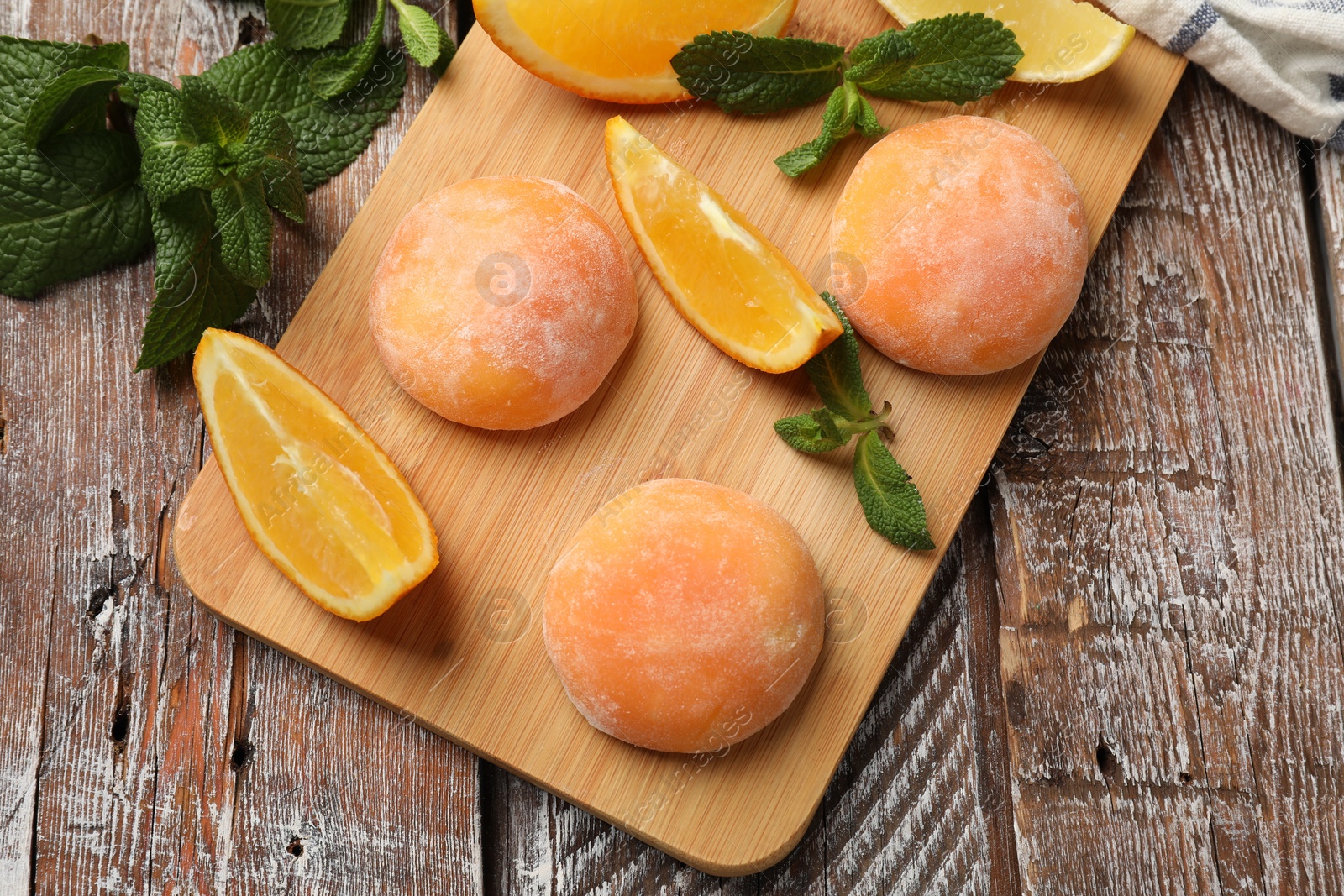 Photo of Board with tasty mochi, cut orange and mint on wooden table, flat lay