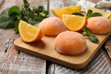 Photo of Board with tasty mochi, cut orange and mint on wooden table, closeup