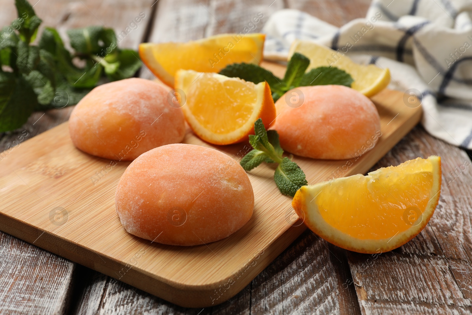 Photo of Board with tasty mochi, cut orange and mint on wooden table, closeup