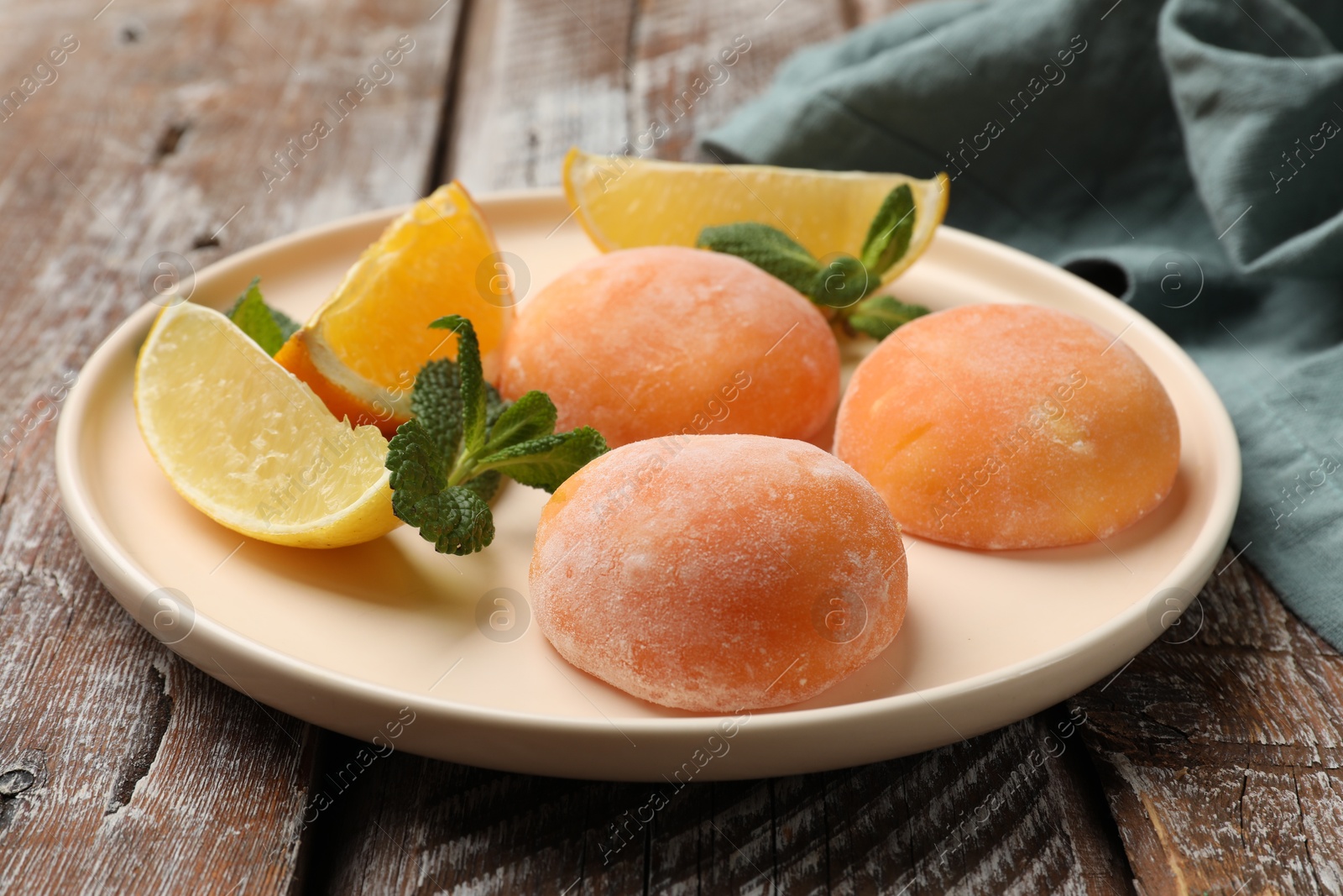 Photo of Plate with tasty mochi, cut orange, lemon and mint on wooden table, closeup