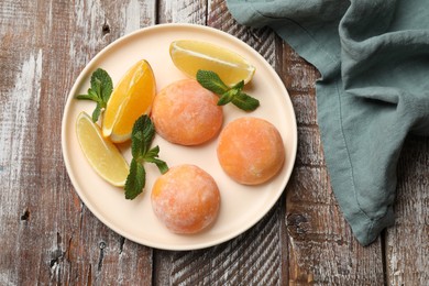 Photo of Plate with tasty mochi, cut orange, lemon and mint on wooden table, top view