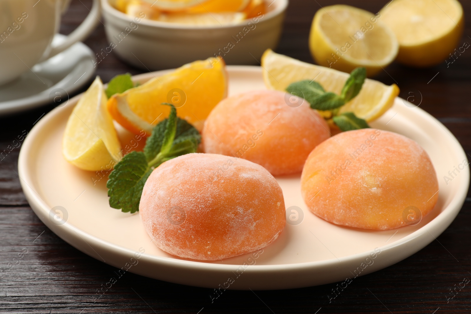 Photo of Plate with tasty mochi, cut orange, lemon and mint on wooden table, closeup