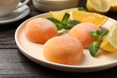 Photo of Plate with tasty mochi, cut orange, lemon and mint on wooden table, closeup