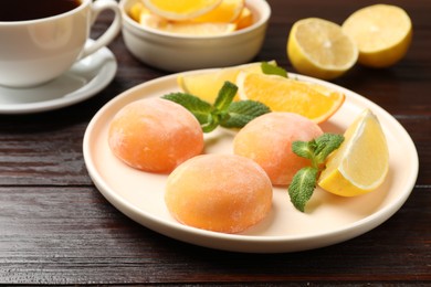 Photo of Plate with tasty mochi, cut orange, lemon and mint on wooden table, closeup