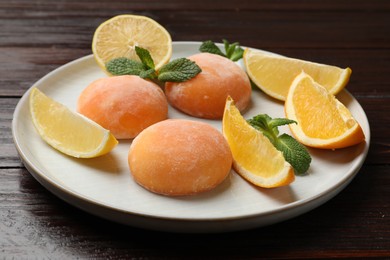 Photo of Plate with tasty mochi, cut orange, lemon and mint on wooden table, closeup