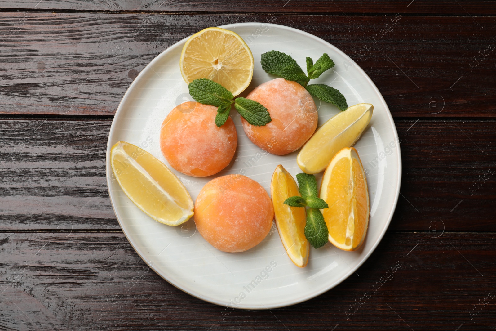 Photo of Plate with tasty mochi, cut orange, lemon and mint on wooden table, top view