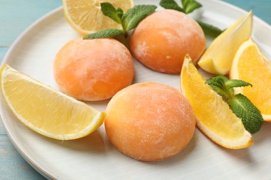 Photo of Plate with tasty mochi, cut orange, lemon and mint on light blue wooden table, closeup