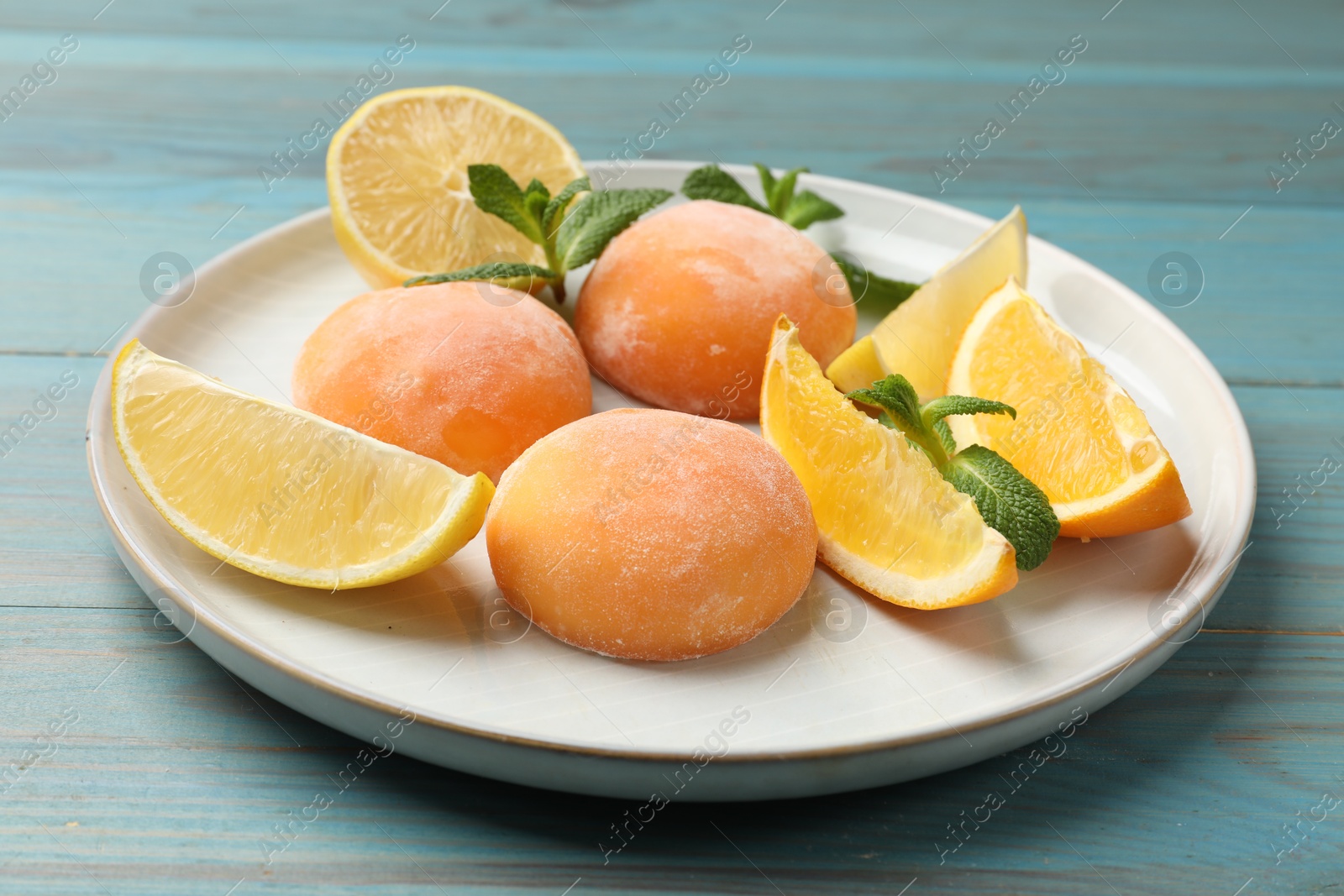 Photo of Plate with tasty mochi, cut orange, lemon and mint on light blue wooden table, closeup