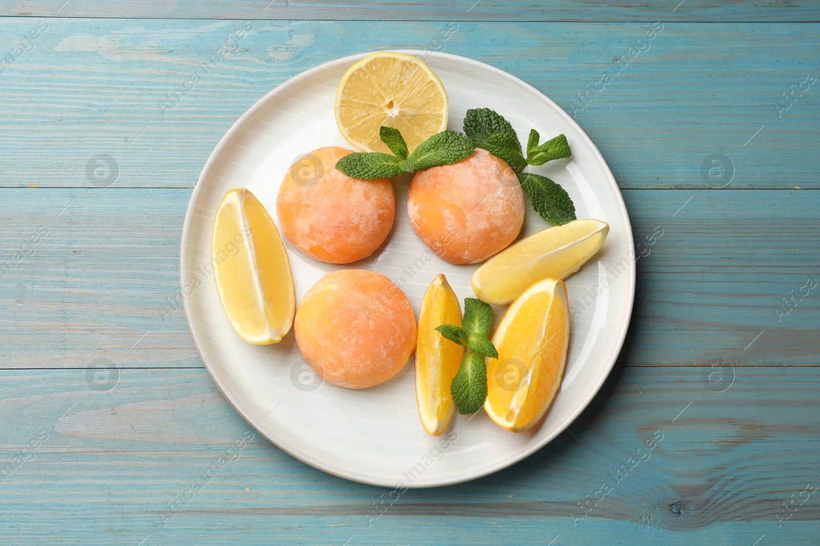 Photo of Plate with tasty mochi, cut orange, lemon and mint on light blue wooden table, top view