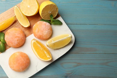 Photo of Tasty mochi, cut orange, lemon and mint on light blue wooden table, top view. Space for text