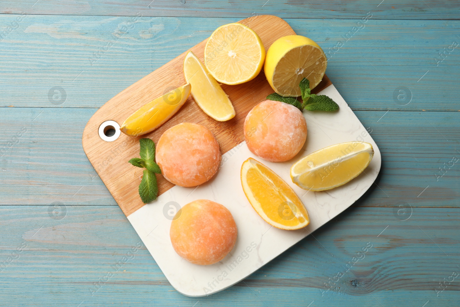 Photo of Board with tasty mochi, cut orange, lemon and mint on light blue wooden table, top view