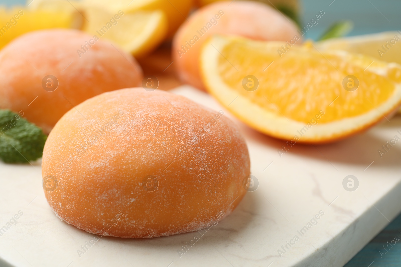 Photo of Board with tasty mochi and cut orange on table, closeup