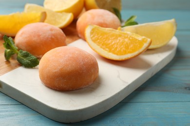 Photo of Board with tasty mochi, cut orange and mint on light blue wooden table, closeup