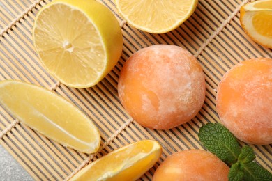 Photo of Bamboo mat with tasty mochi, cut orange, lemon and mint on grey textured table, flat lay