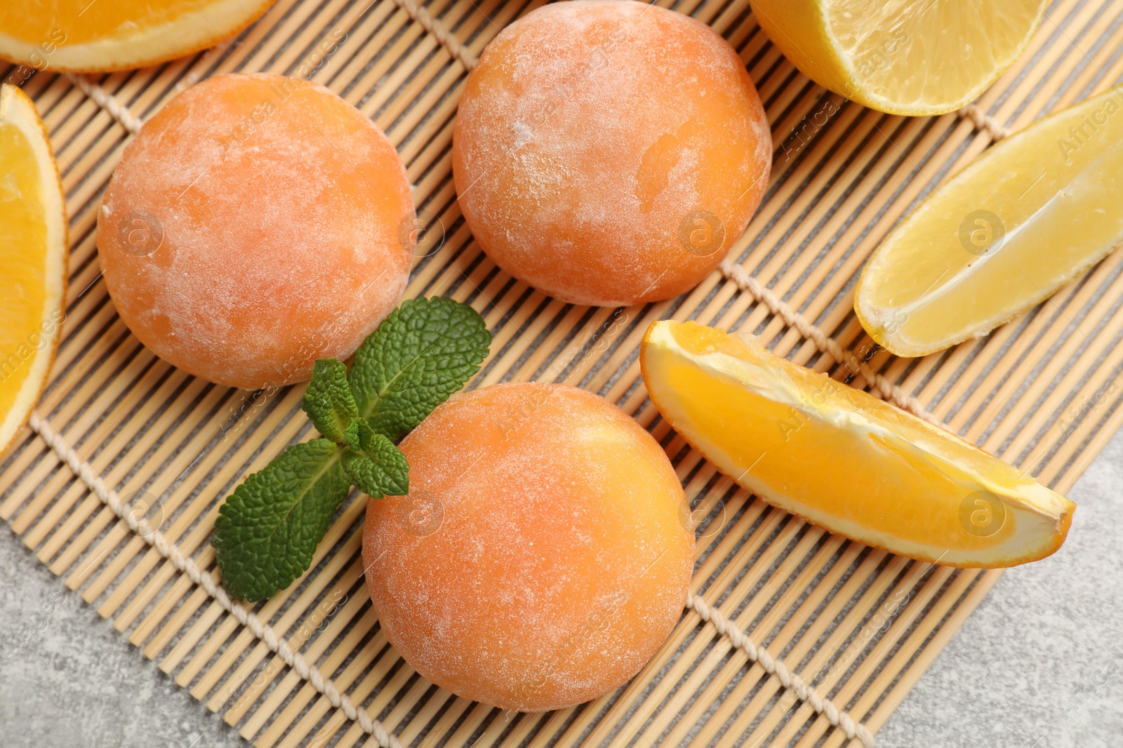 Photo of Bamboo mat with tasty mochi, cut orange, lemon and mint on grey textured table, flat lay