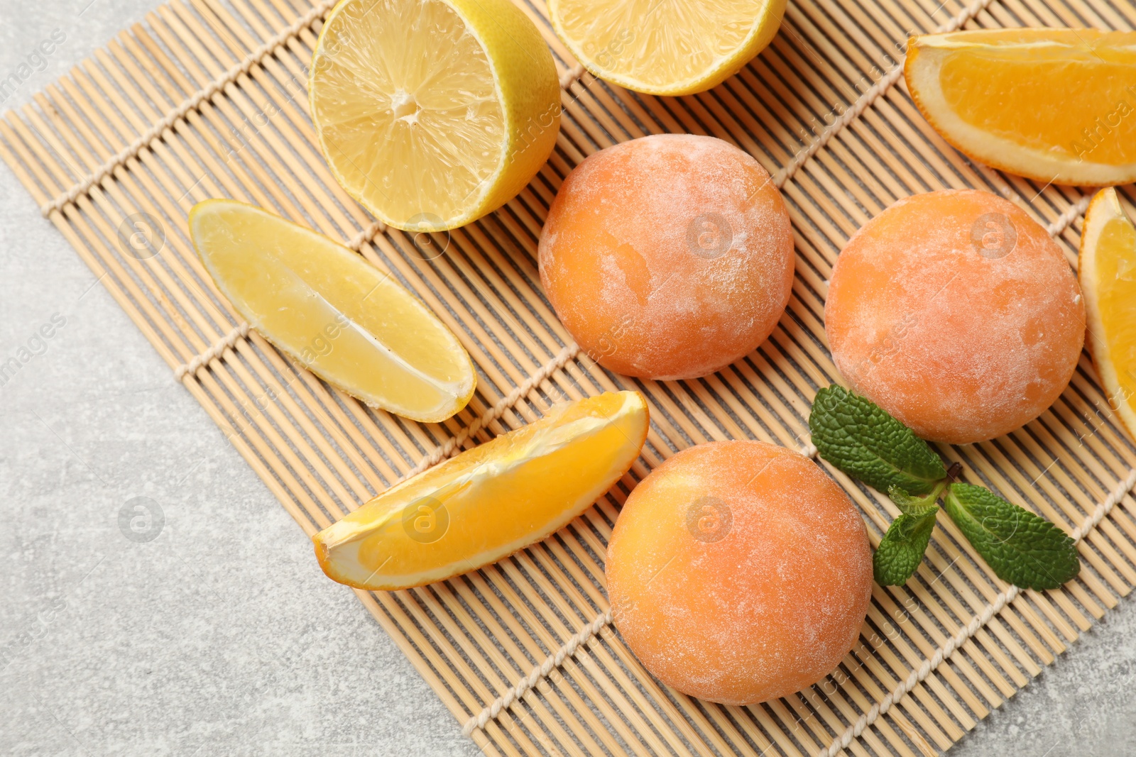 Photo of Bamboo mat with tasty mochi, cut orange, lemon and mint on grey textured table, flat lay