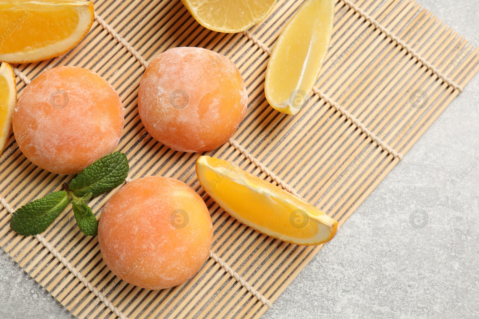 Photo of Bamboo mat with tasty mochi, cut orange, lemon and mint on grey textured table, flat lay