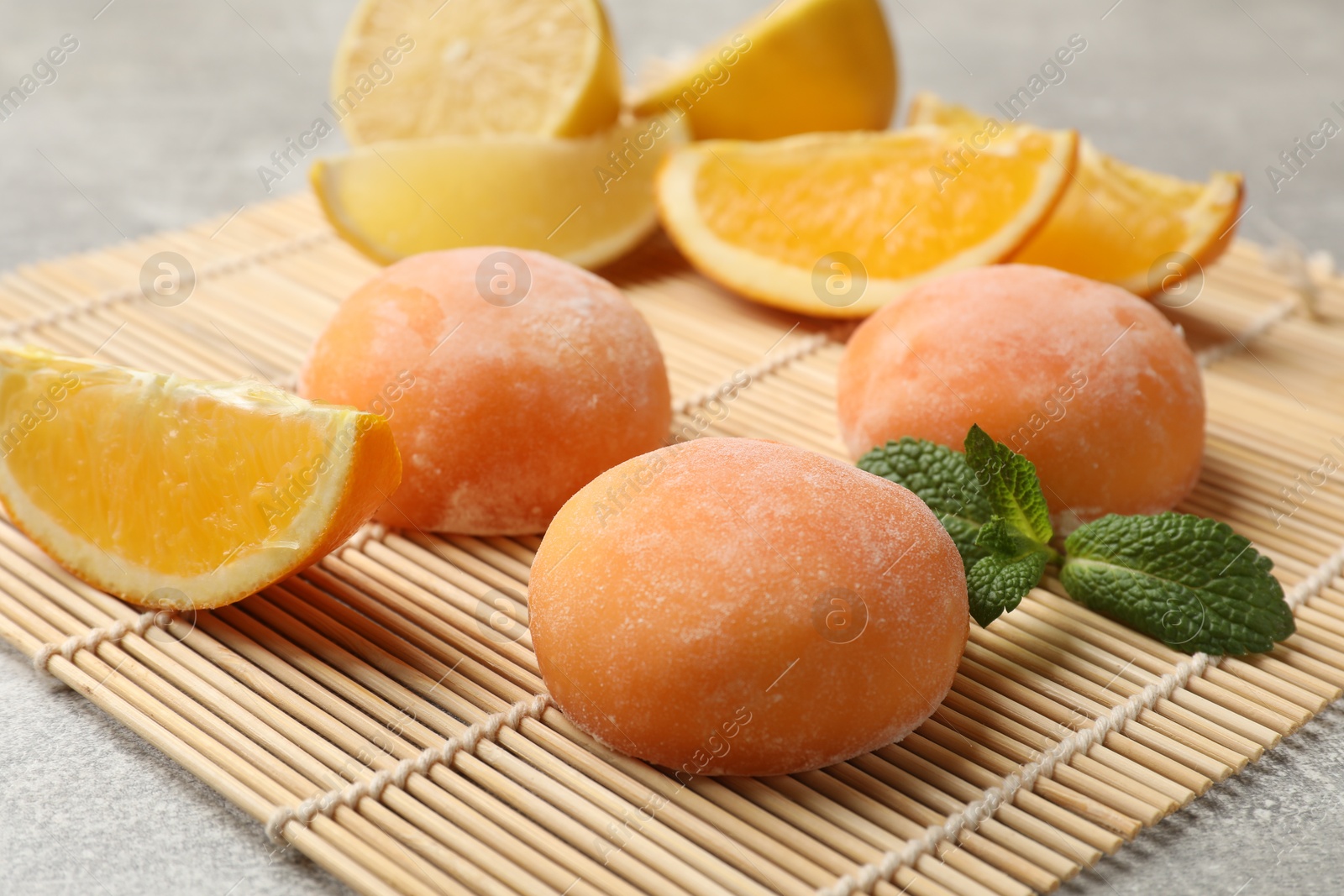 Photo of Bamboo mat with tasty mochi, cut orange and mint on grey textured table, closeup