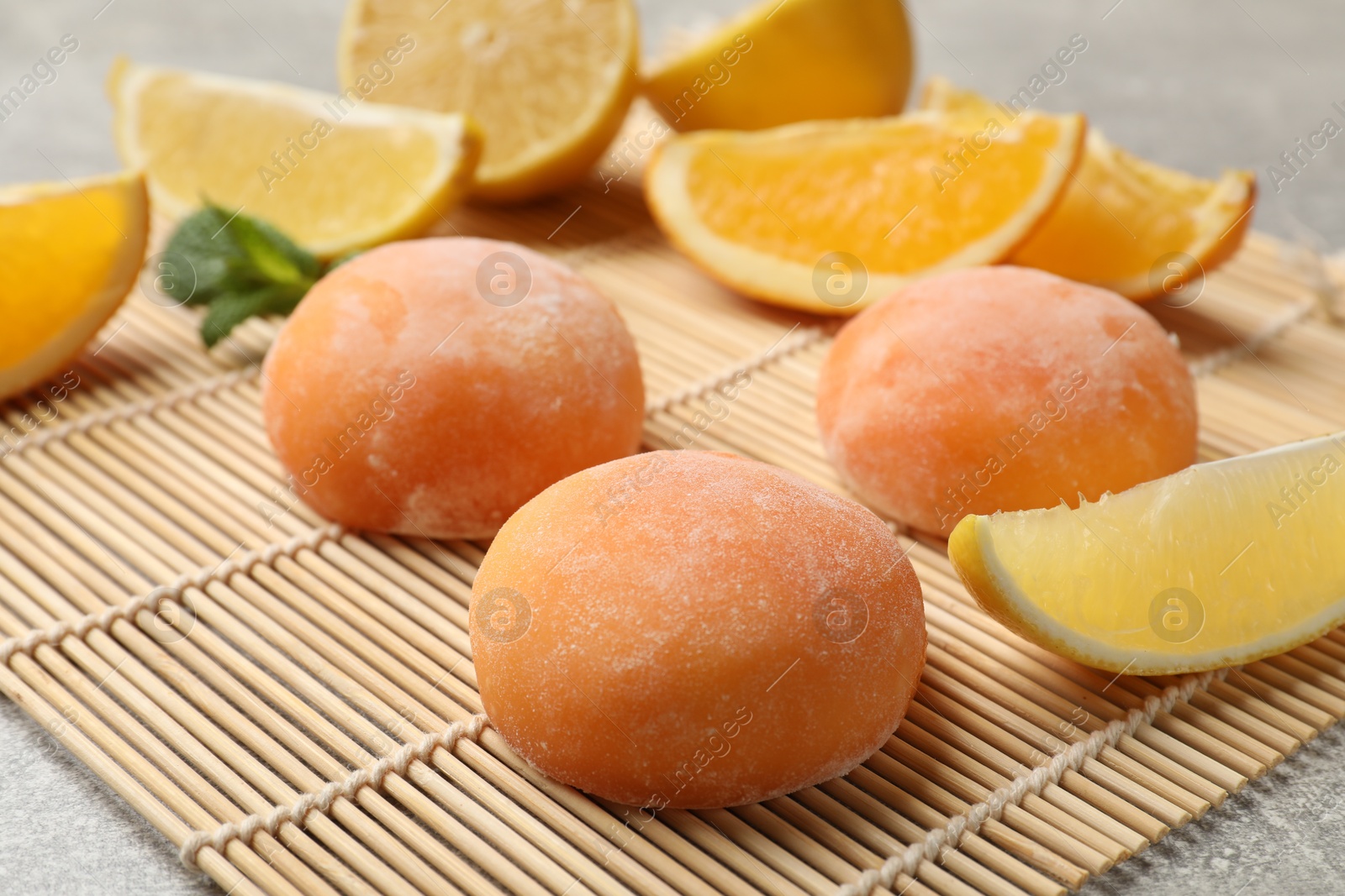 Photo of Bamboo mat with tasty mochi, cut orange, lemon and mint on grey textured table, closeup