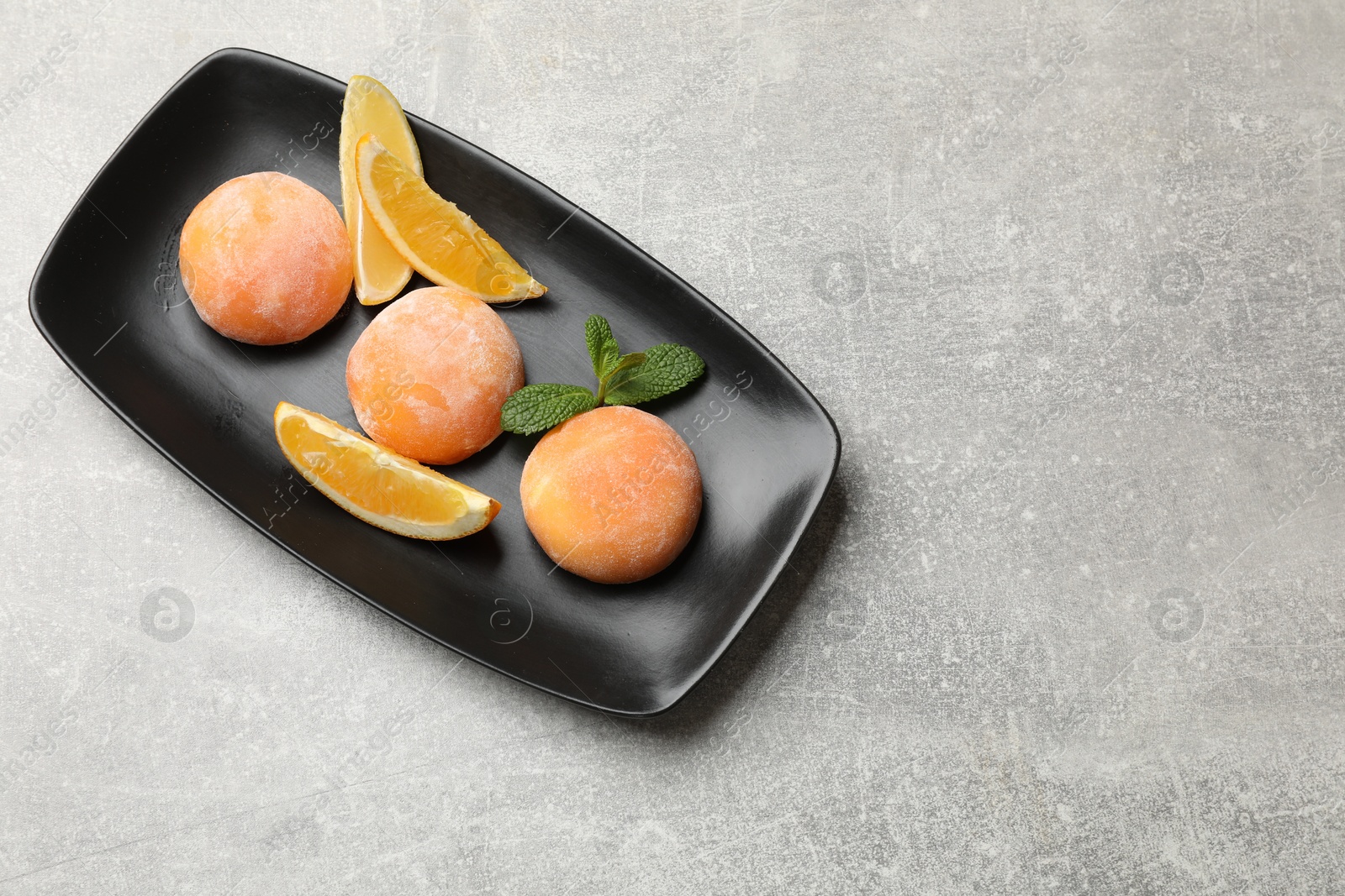 Photo of Tasty mochi, cut orange and mint on grey textured table, top view. Space for text