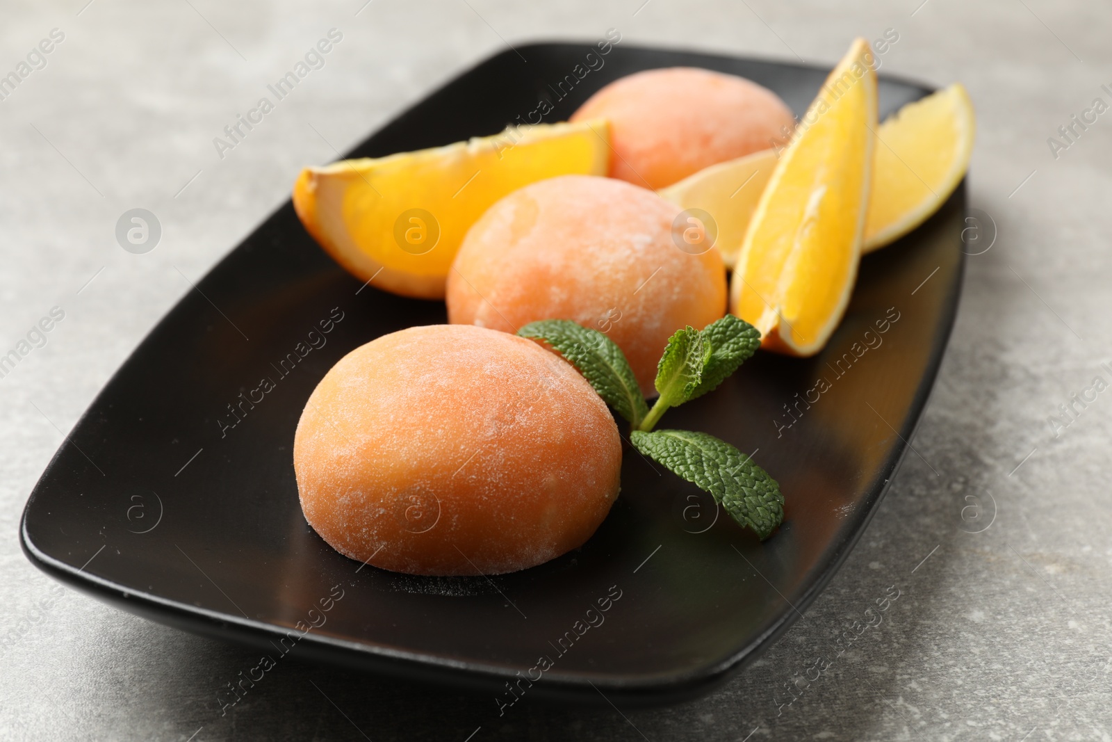 Photo of Tasty mochi, cut orange and mint on grey textured table, closeup