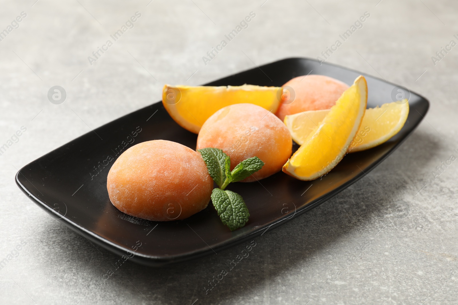 Photo of Tasty mochi, cut orange and mint on grey textured table, closeup