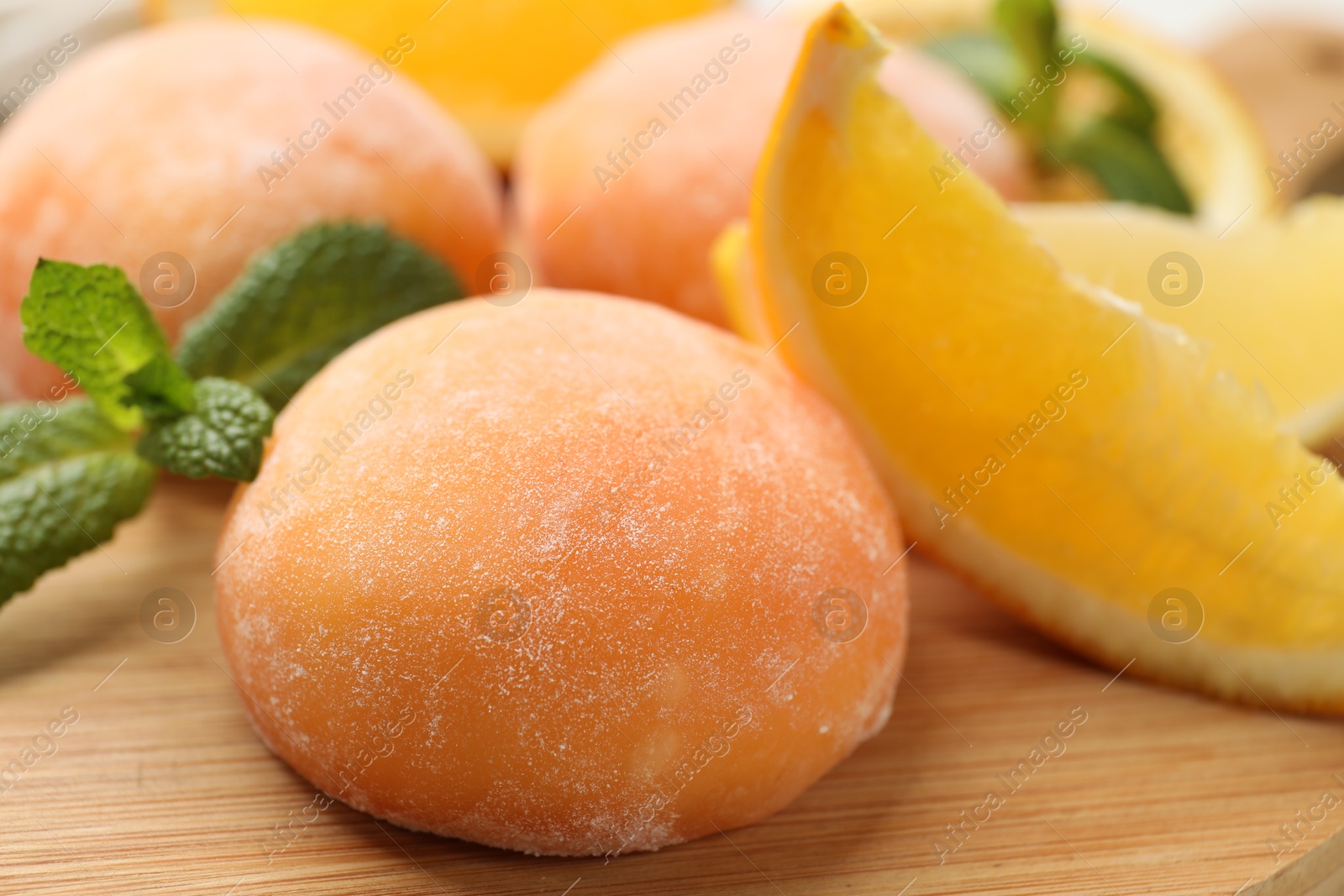 Photo of Tasty mochi, cut orange and mint on wooden board, closeup