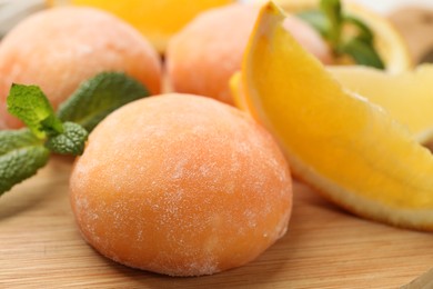 Photo of Tasty mochi, cut orange and mint on wooden board, closeup