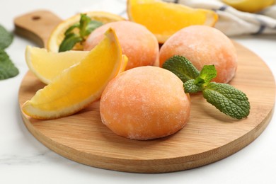 Photo of Board with tasty mochi, cut orange and mint on white table, closeup