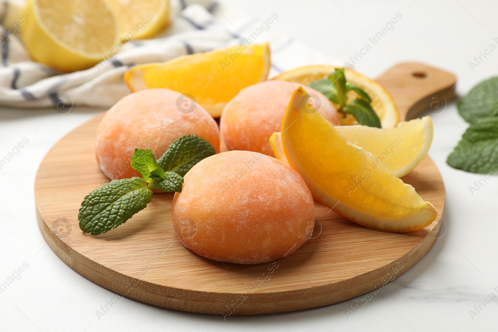 Photo of Board with tasty mochi, cut orange and mint on white table, closeup