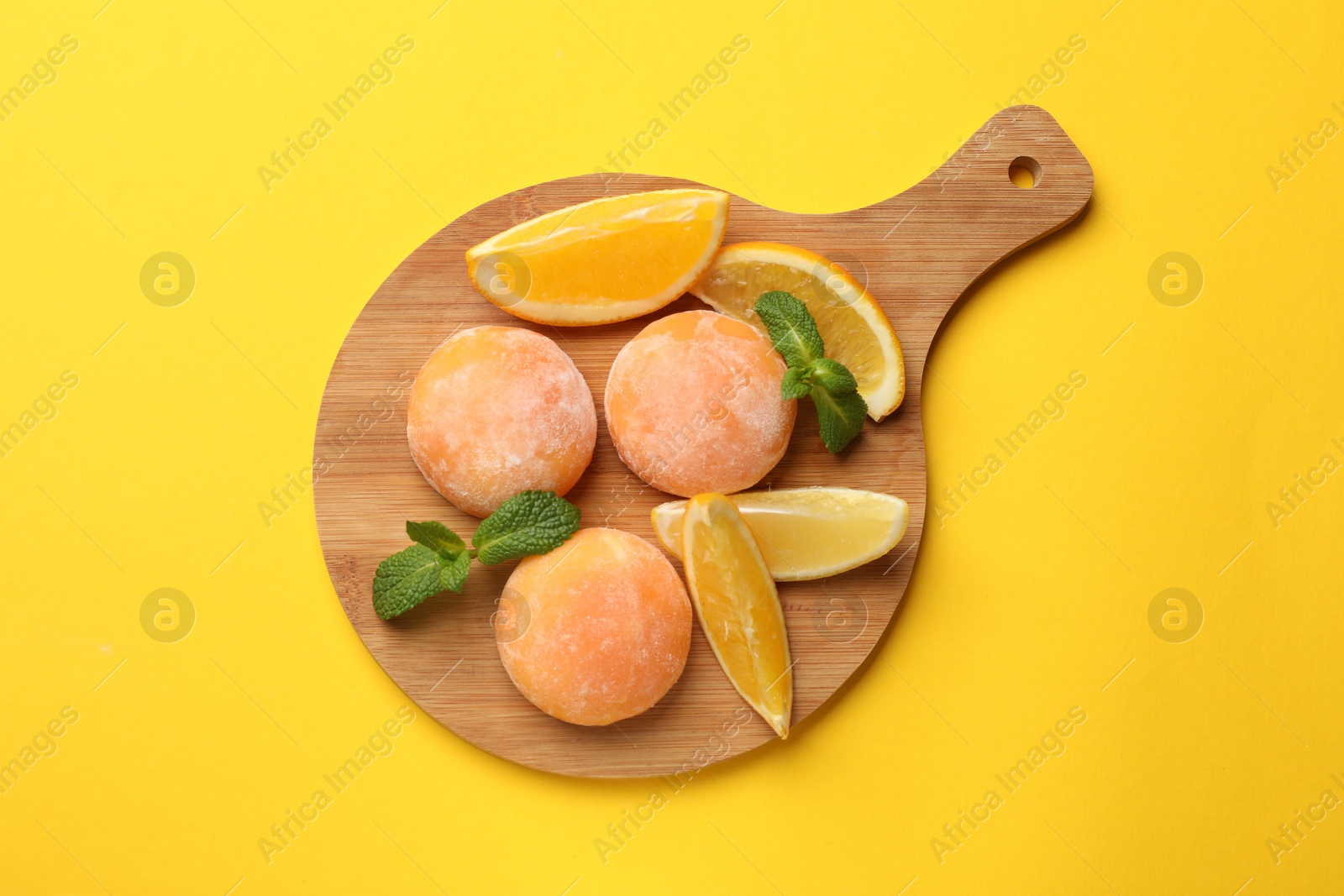 Photo of Board with tasty mochi, cut orange and mint on yellow table, top view