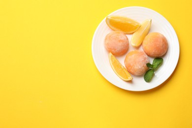 Photo of Plate with tasty mochi, cut orange and mint on yellow table, top view. Space for text