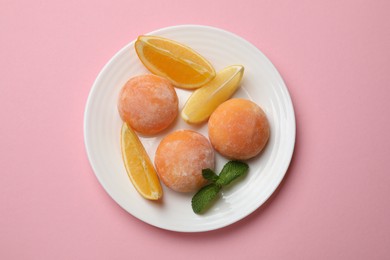 Photo of Plate with tasty mochi, cut orange and mint on pink table, top view