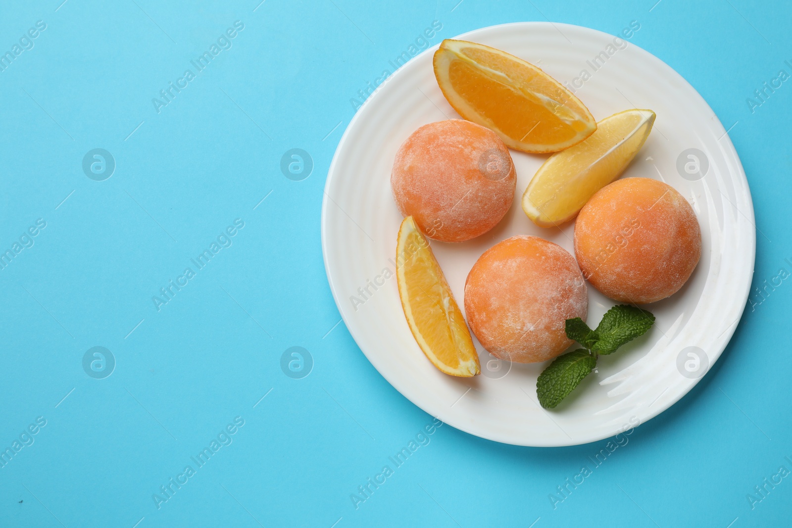 Photo of Plate with tasty mochi, cut orange and mint on light blue table, top view. Space for text